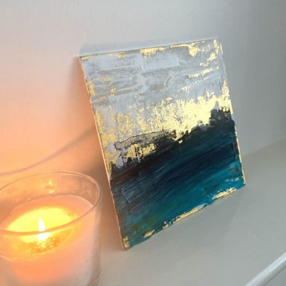 Blue white and gold painting on a mantlepiece next to a lit candle