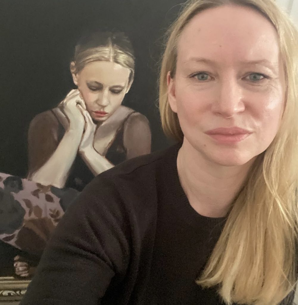 a blonde haired woman in front of a portrait of a sad girl